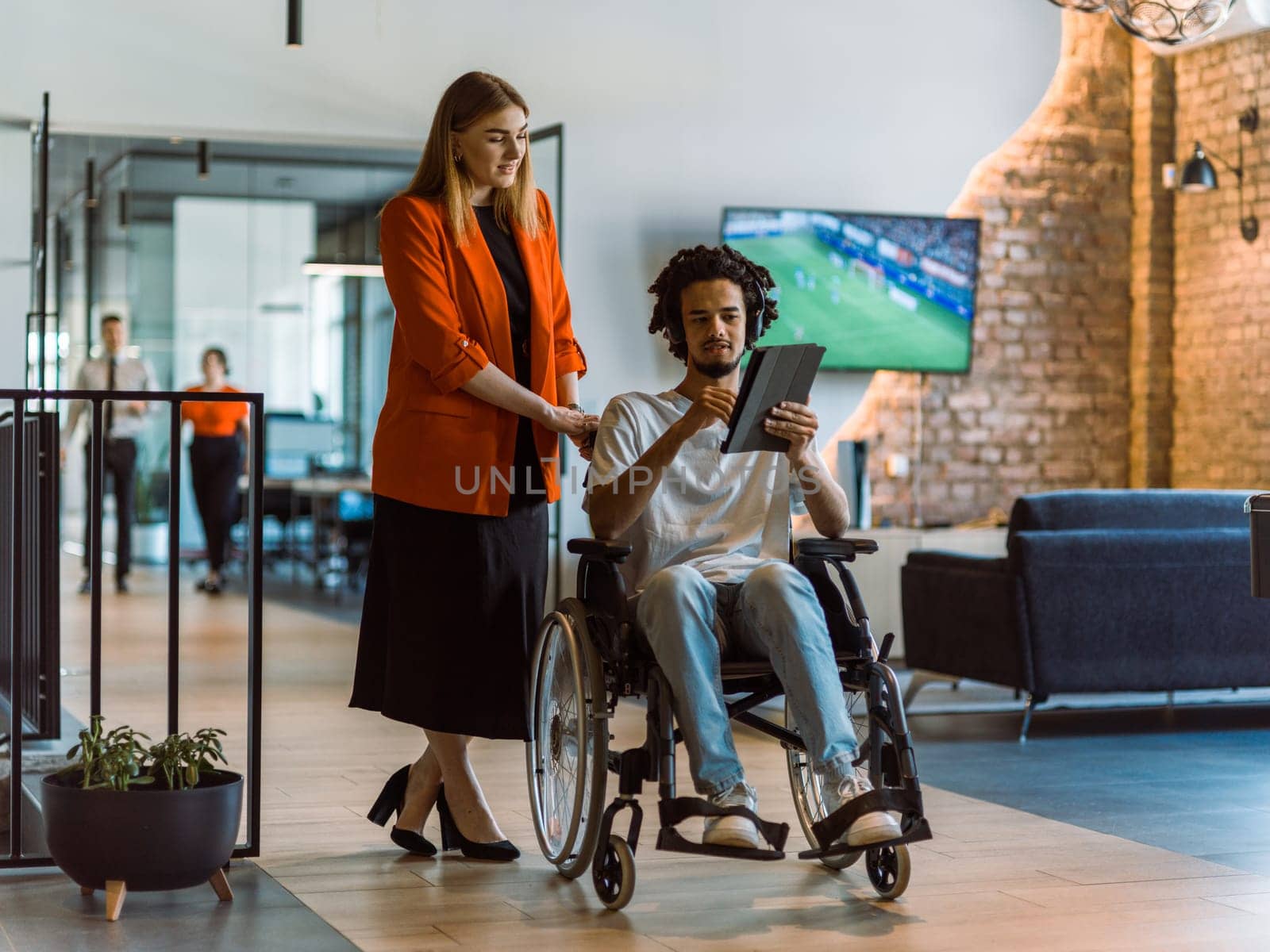African-American businessman in a wheelchair engages in a collaborative discussion, using a tablet, with his business colleague, exemplifying the seamless integration of adaptive technology and fostering diversity in a modern corporate environment.