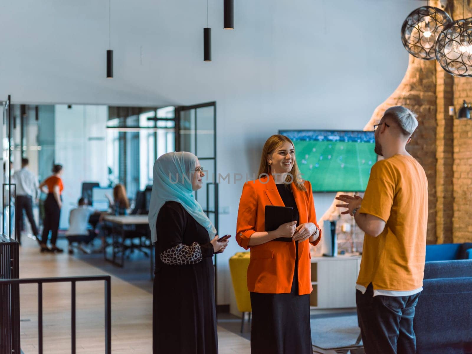 A group of young business colleagues, including a woman in a hijab, stands united in the modern corridor of a spacious startup coworking center, representing diversity and collaborative spirit.