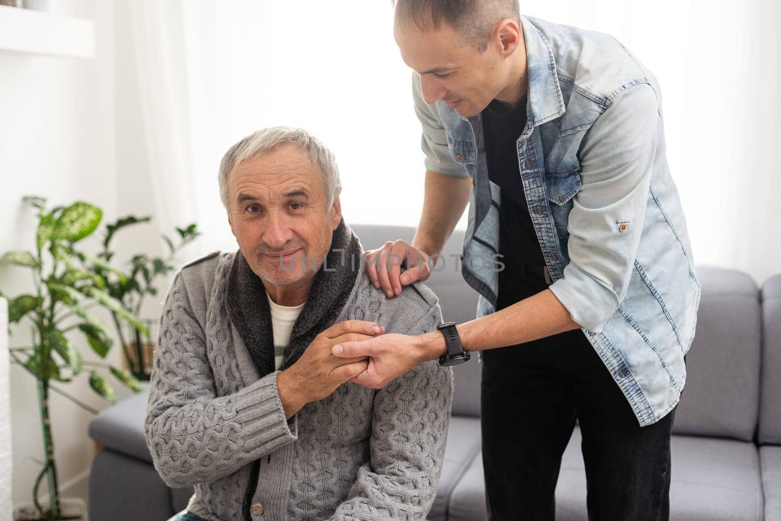 Grown up son asking for apologizes to offended stressed elderly senior daddy, sitting together on couch. Compassionate young man supporting, giving psychological help to frustrated middle aged father. High quality photo