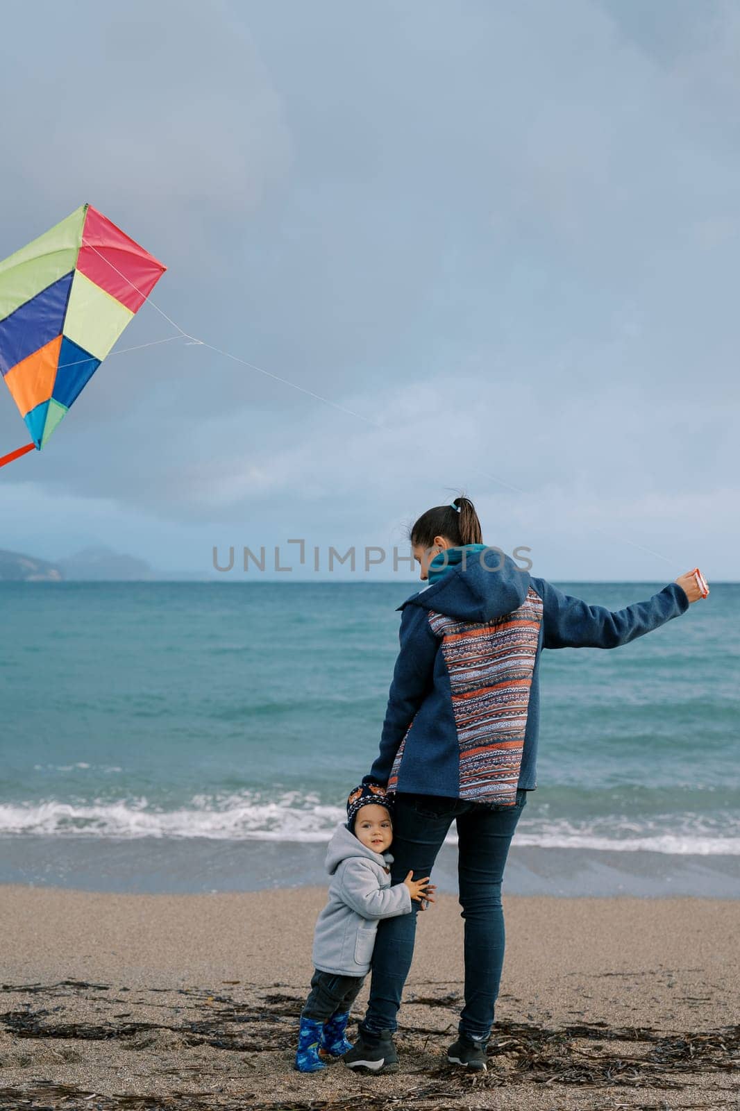 Little girl hugs her mother leg on the beach with a kite. Back view. High quality photo