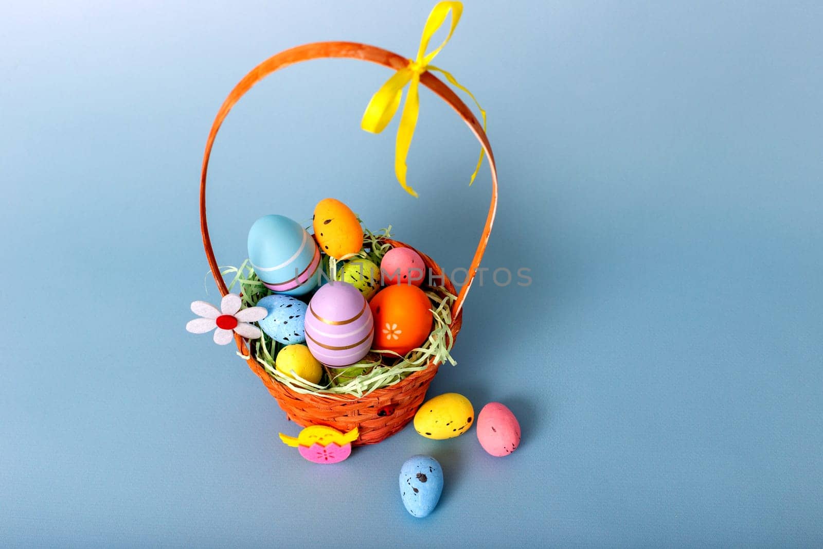 Top view of wicker basket filled with decorative multi colored easters eggs on a light blue background.
