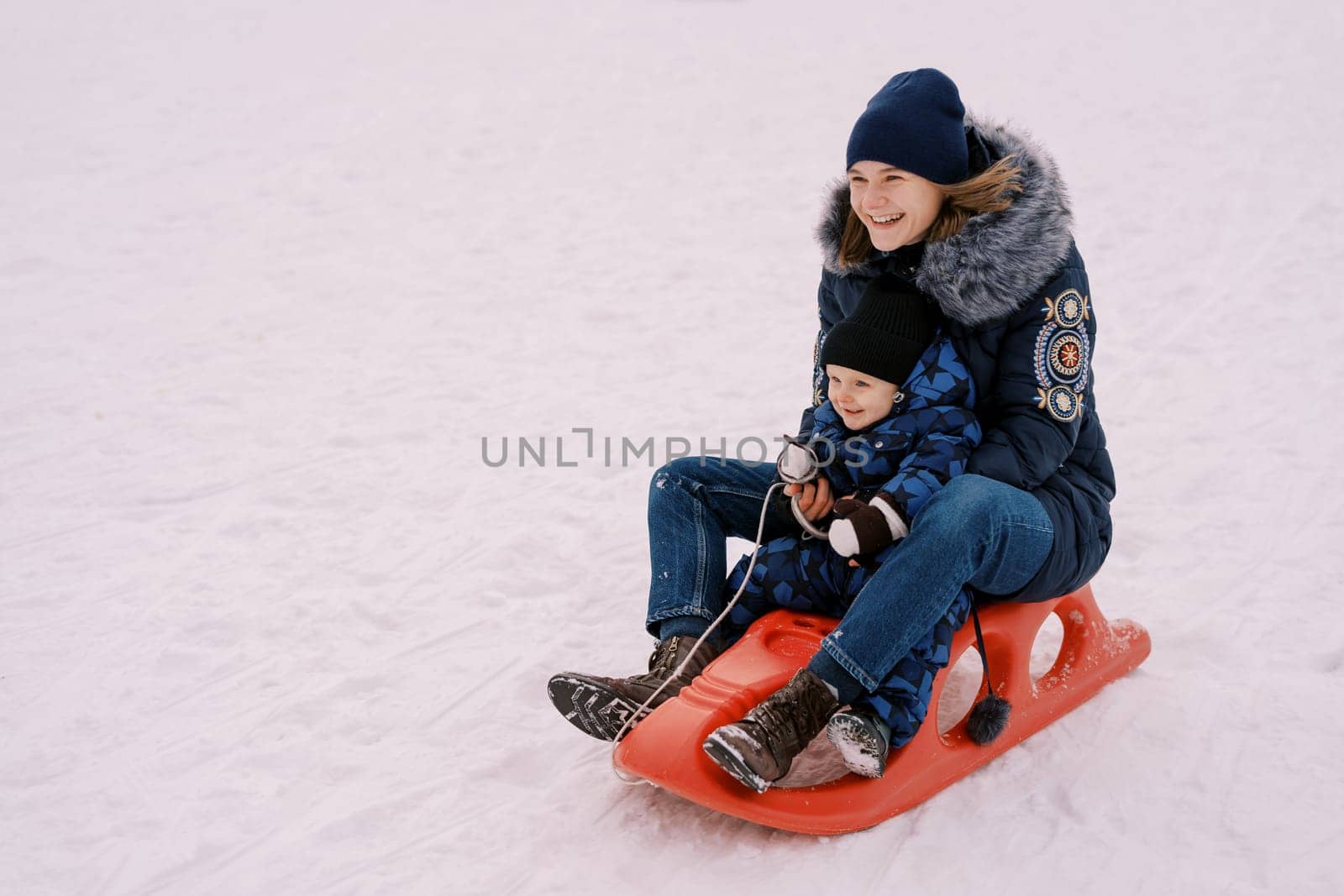 Laughing mother with a little boy rides a sled down the mountain. High quality photo