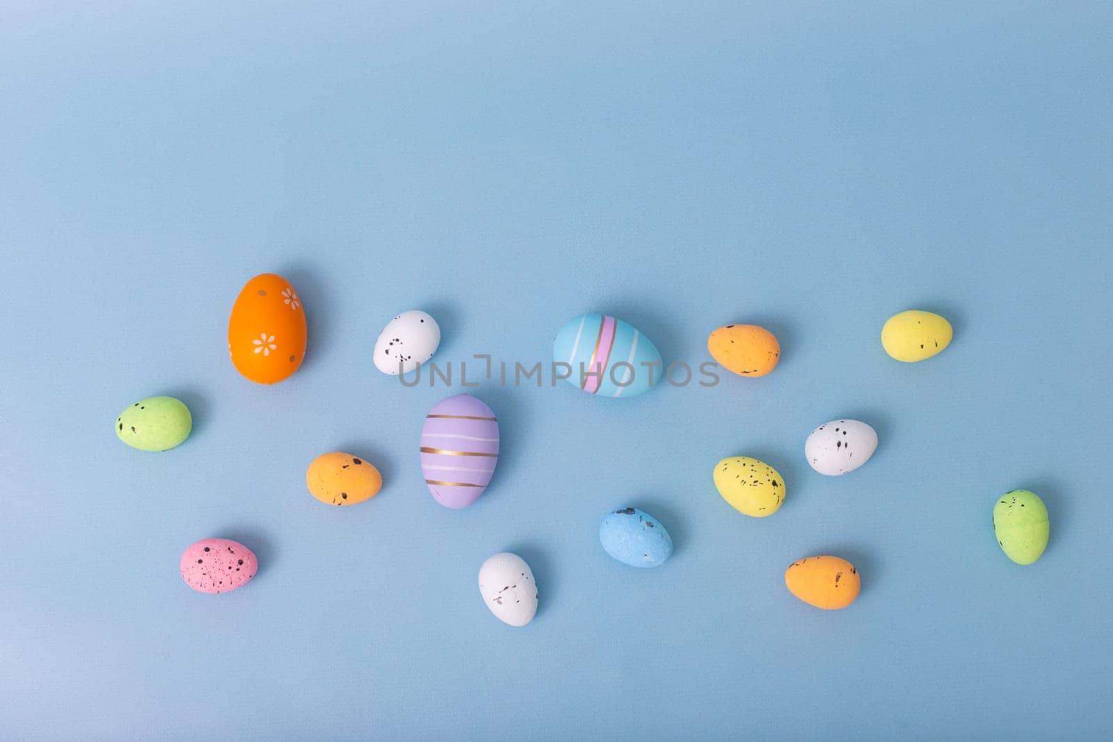decorative multicolored eggs are scattered on a light blue background, top view.