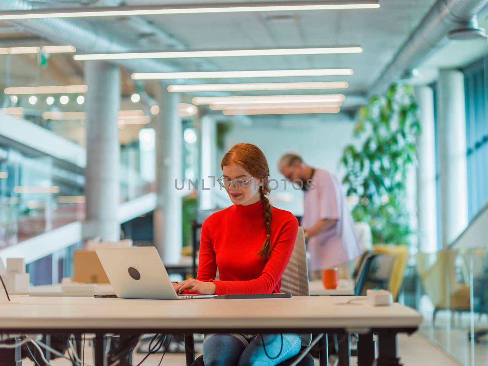 In a modern startup office, a professional businesswoman with orange hair sitting at her laptop, epitomizing innovation and productivity in her contemporary workspace by dotshock