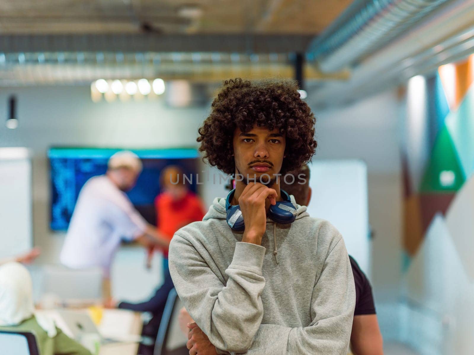 In a modern office environment, an African American young entrepreneur with headphones engages in work, while in the background, his dedicated colleagues exemplify teamwork and collaboration, encapsulating the essence of contemporary corporate success by dotshock
