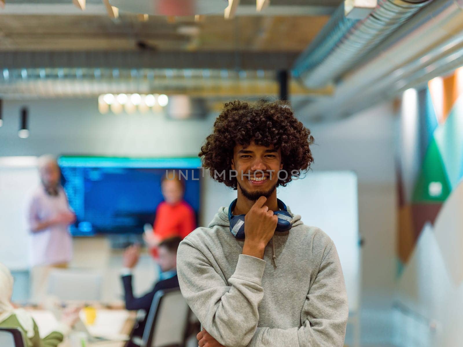 In a modern office environment, an African American young entrepreneur with headphones engages in work, while in the background, his dedicated colleagues exemplify teamwork and collaboration, encapsulating the essence of contemporary corporate success.