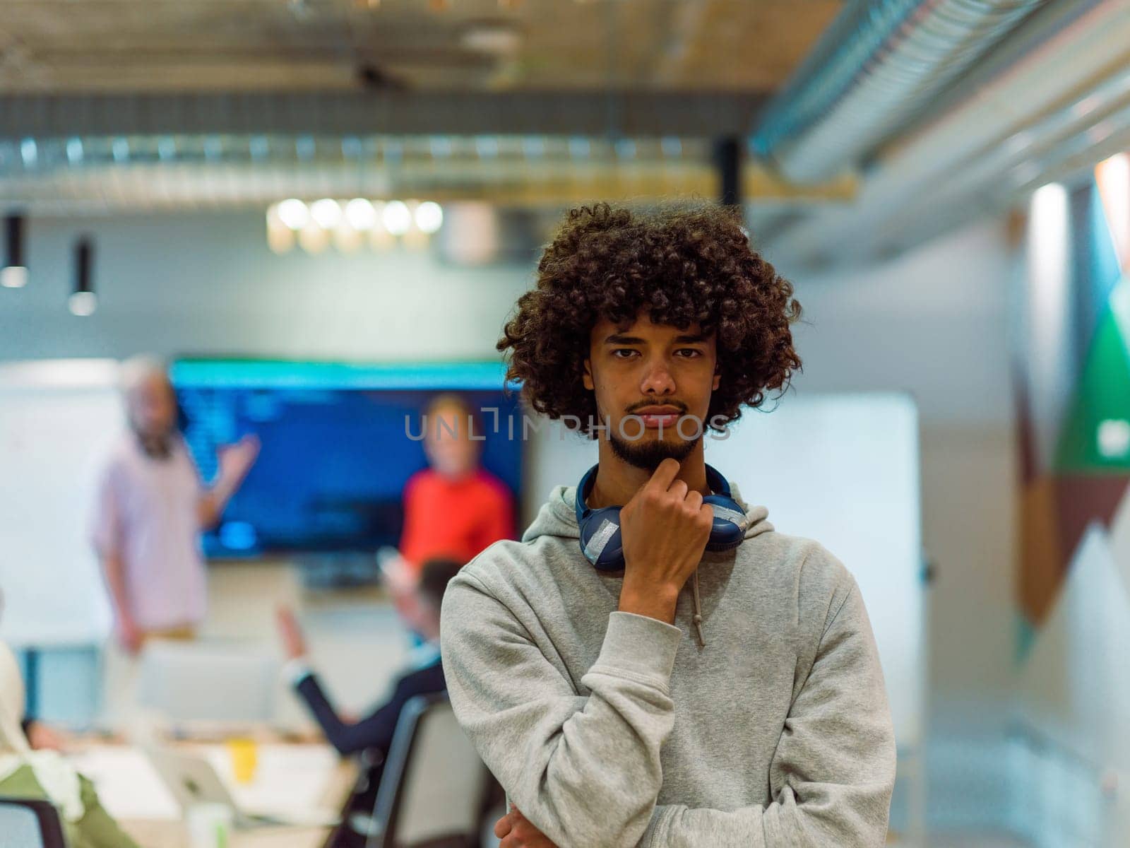 In a modern office environment, an African American young entrepreneur with headphones engages in work, while in the background, his dedicated colleagues exemplify teamwork and collaboration, encapsulating the essence of contemporary corporate success by dotshock