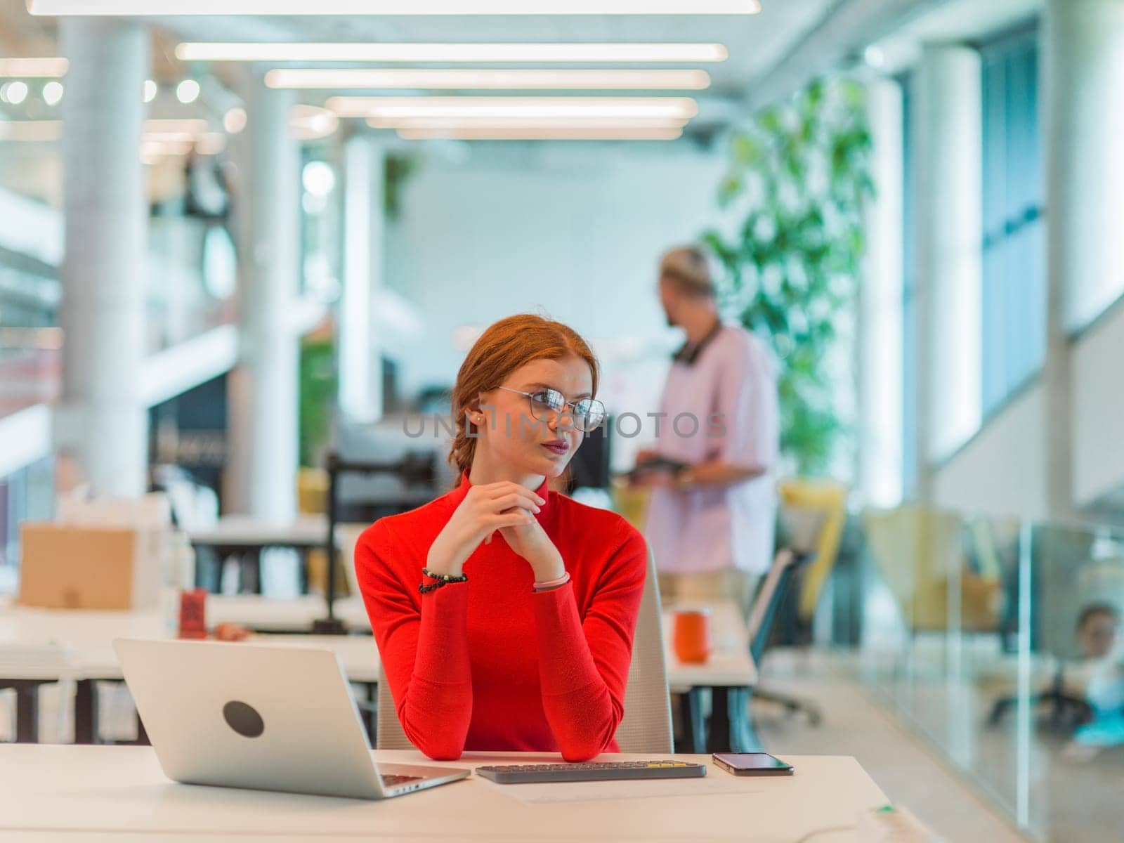 In a modern startup office, a professional businesswoman with orange hair sitting at her laptop, epitomizing innovation and productivity in her contemporary workspace by dotshock