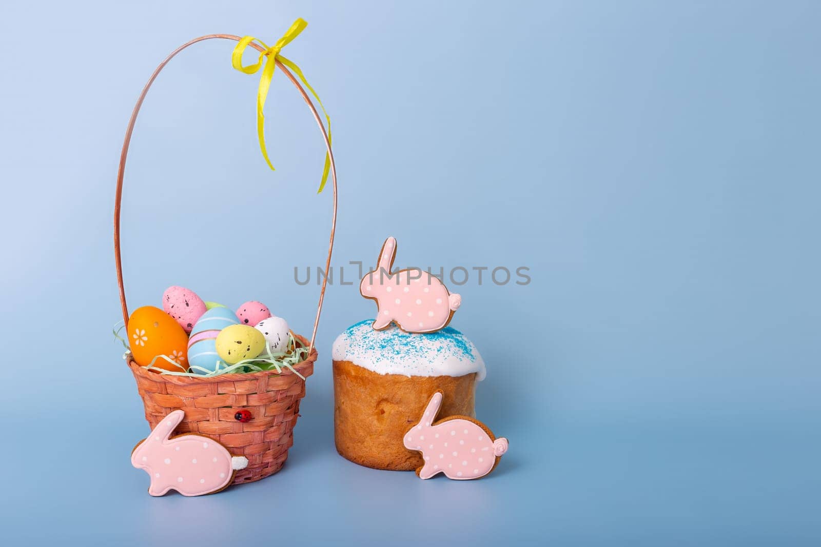 Cute pink gingerbread in the form of a rabbit , an Easter cake and a basket with decorative multicolored eggs stand on a blue background.