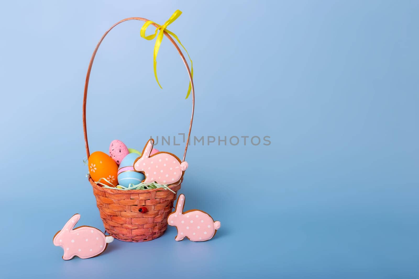 Cute pink gingerbread in the form of a rabbit and a basket with decorative Easter eggs stand on a blue background