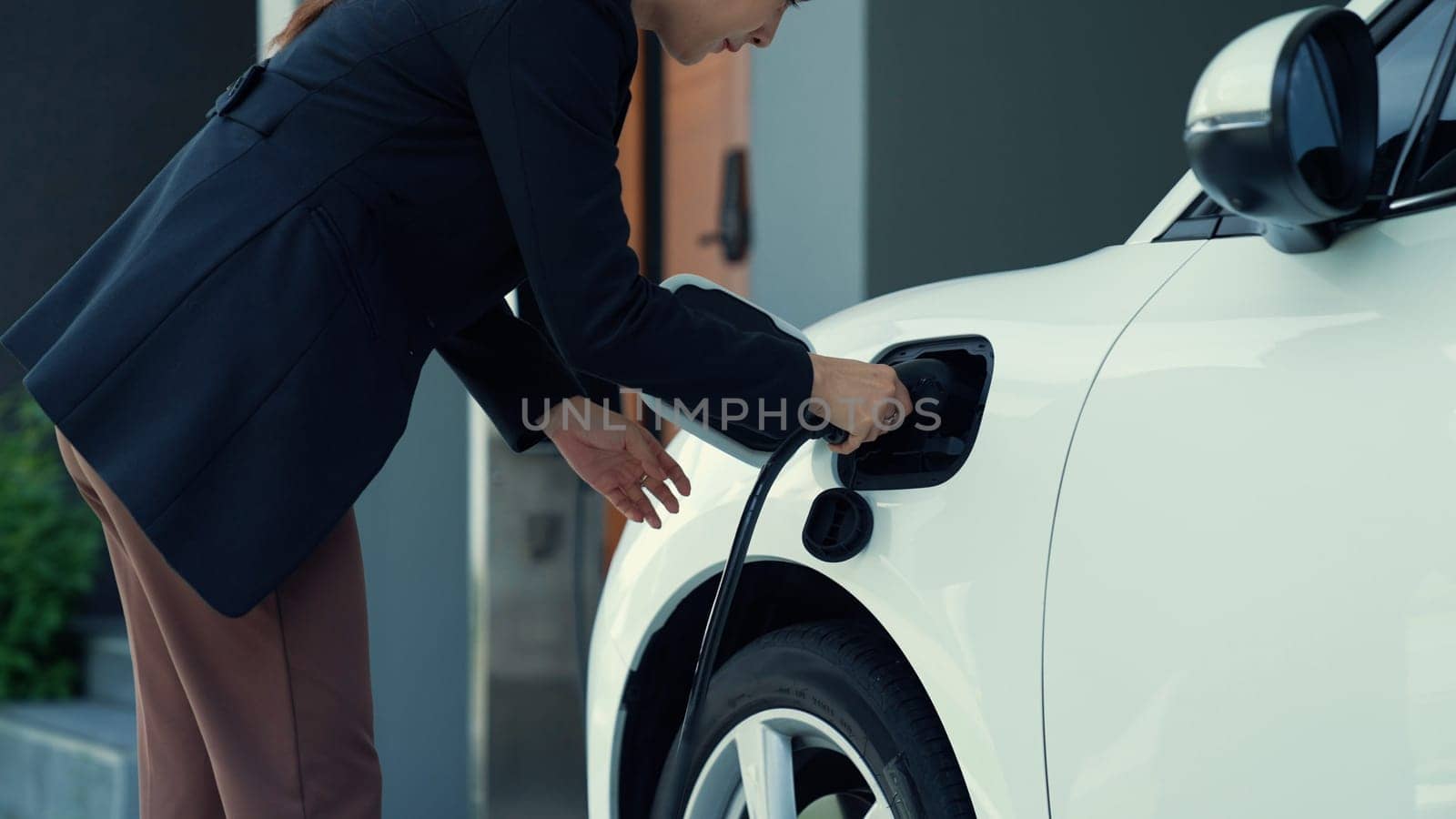 Progressive woman unplugs the electric vehicle's charger at his residence. by biancoblue