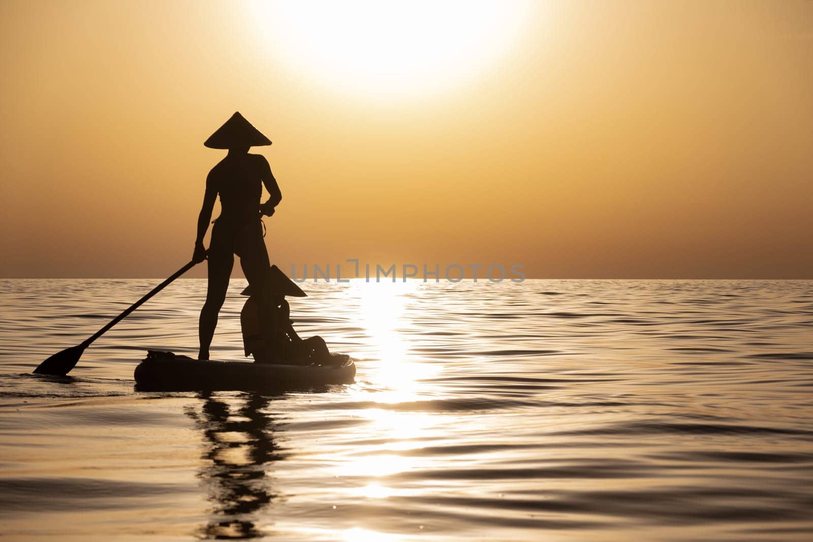 woman with a child on a sup board in the sea swim against the background of a beautiful sunset, Standup paddleboarding