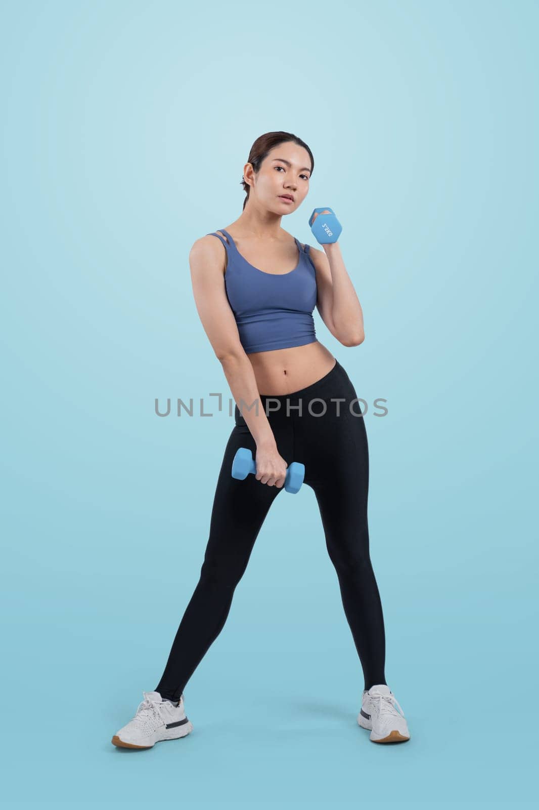 Vigorous energetic woman doing dumbbell weight lifting exercise on isolated background. Young athletic asian woman strength and endurance training session as body workout routine.