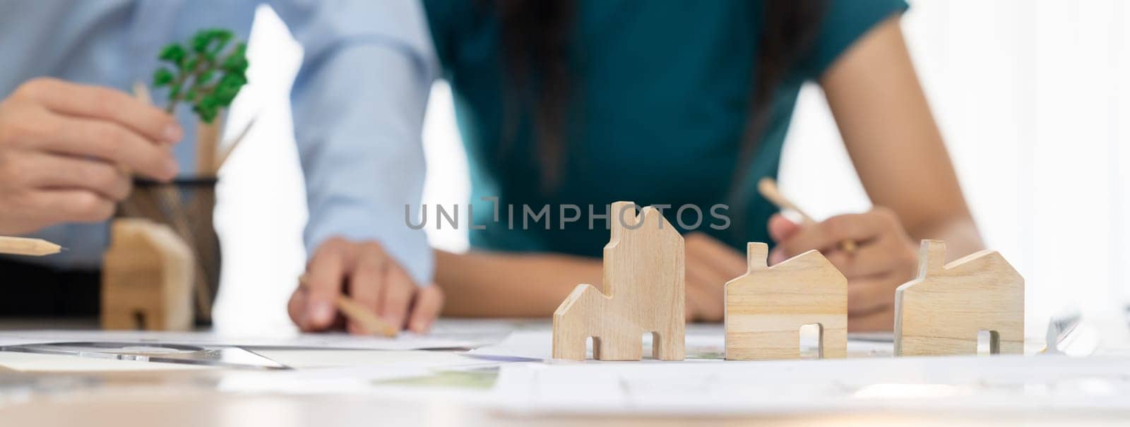 Professional architect engineer team discussion about architectural project on meeting table with wooden block and blueprint scatter around. Design and cooperate concept. Closeup. Delineation.