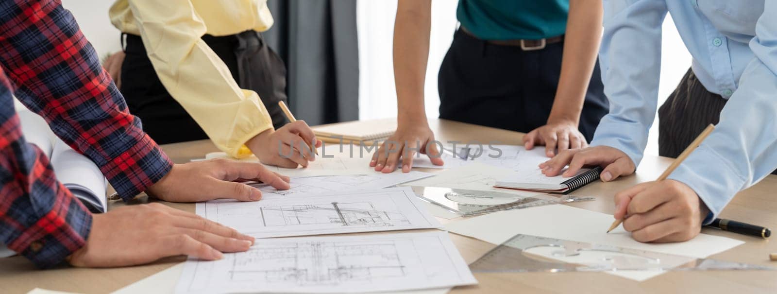 Skilled architect engineer team discuss about architectural project while project manager using laptop analysis data at meeting table with architectural document scatter around. Closeup. Delineation.