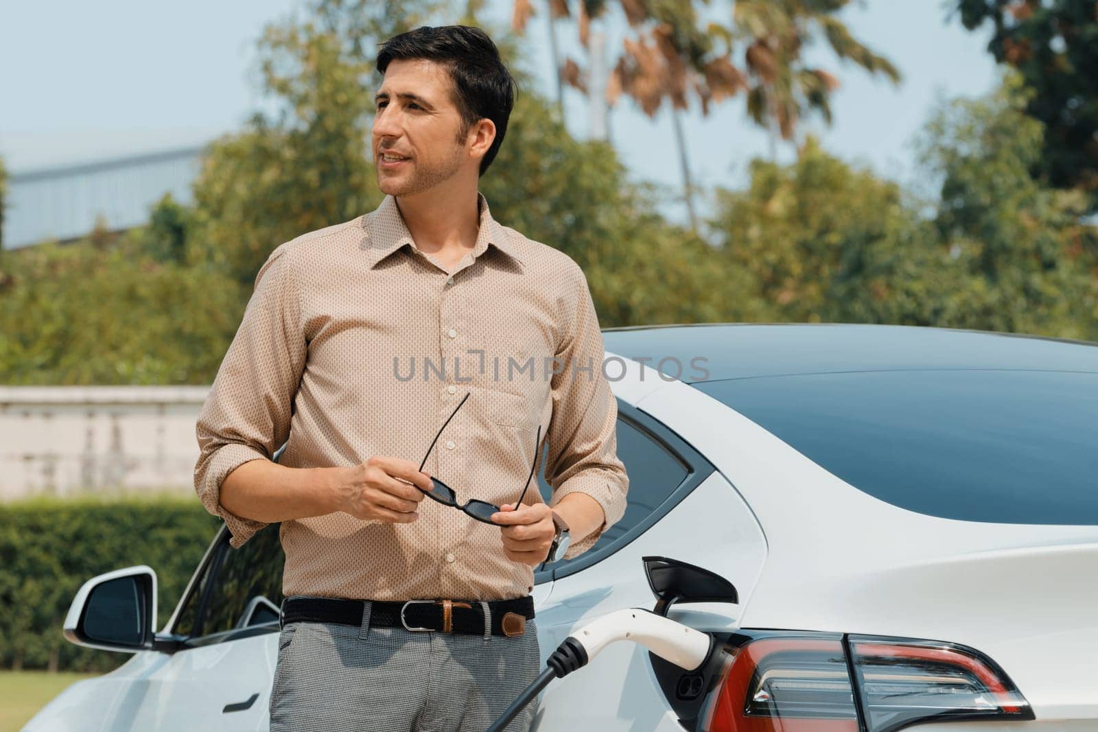 Young man recharge electric car's battery from charging station. Expedient by biancoblue