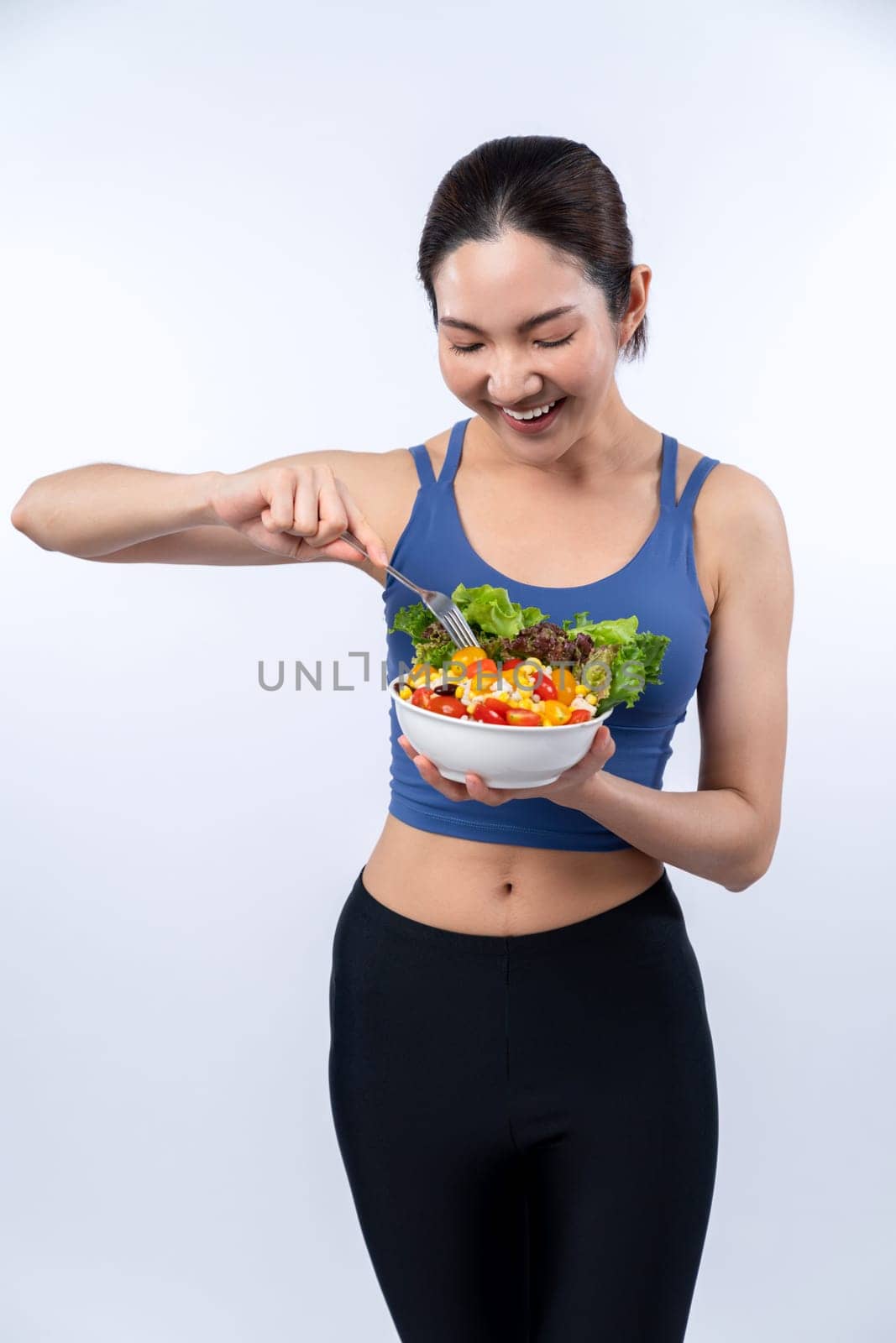 Young sporty Asian woman in sportswear holding salad bowl fill with vibrant of fruit and vegetable. Natural youthful and fit body lifestyle with balance nutrition on isolated background. Vigorous