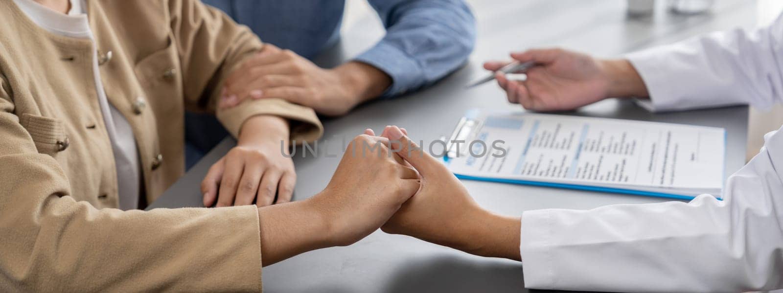 Doctor providing compassionate healthcare consultation while young couple patient holding hand, comfort each other after infertile report. Reproductive and medical fertility consulting. Neoteric