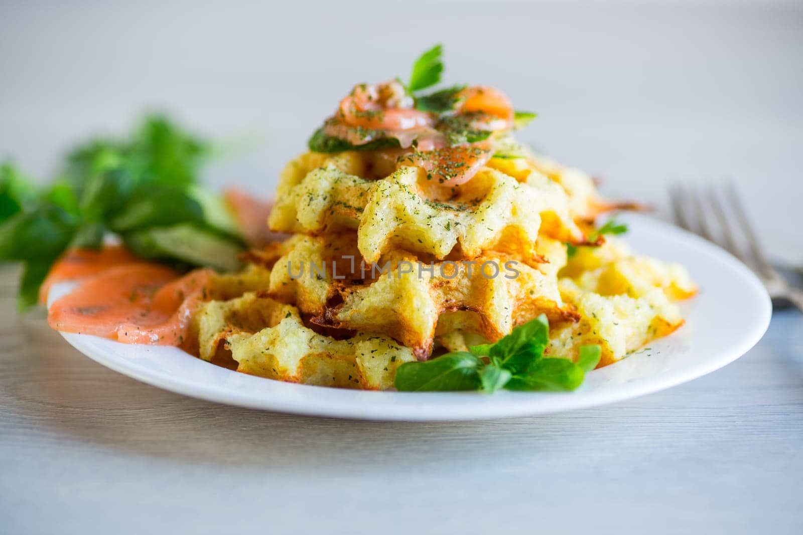 Cooked potato waffles with lightly salted red fish and herbs in a plate, on a wooden table.