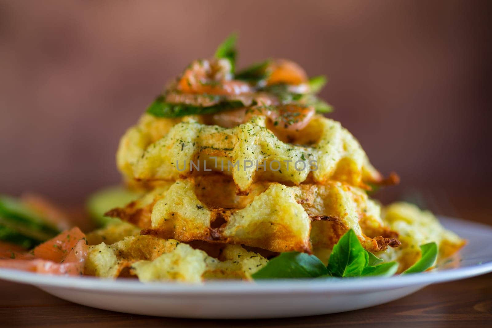 Cooked potato waffles with lightly salted red fish and herbs in a plate, on a wooden table.