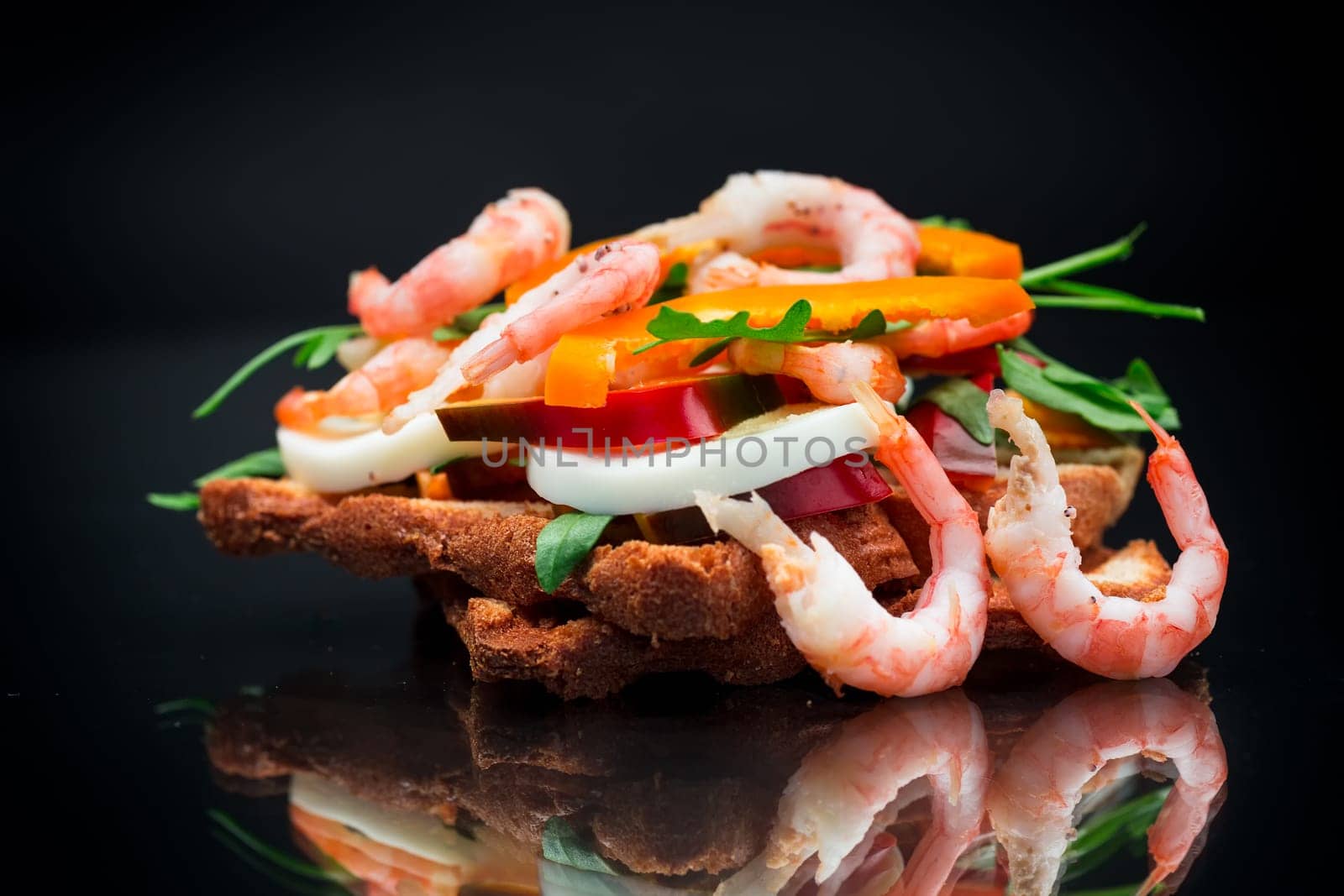 cooked sandwich with shrimp, eggs, pepper and greens, isolated on black background