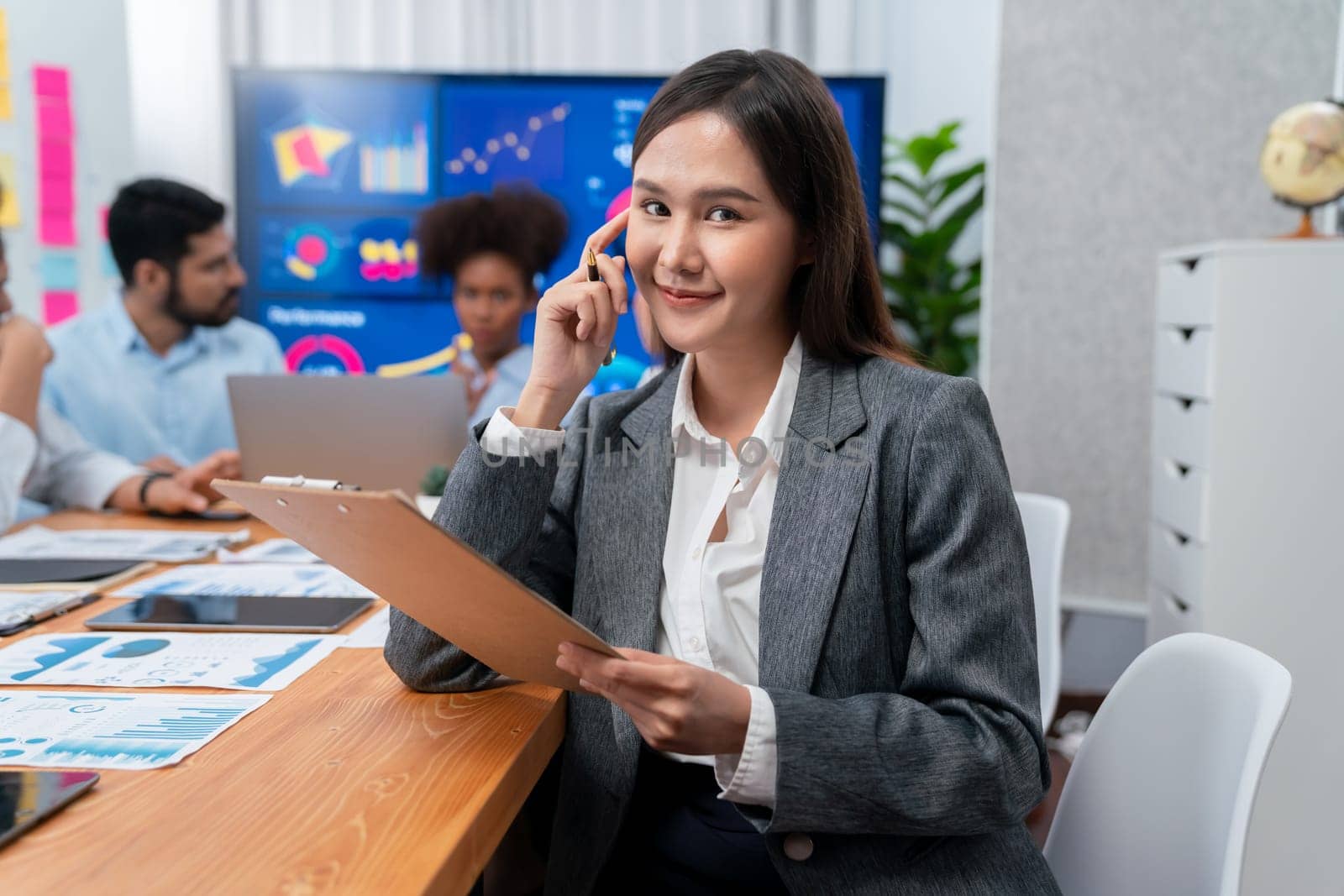 Portrait of happy young asian businesswoman with group of office worker on meeting with screen display business dashboard in background. Confident office lady at team meeting. Concord