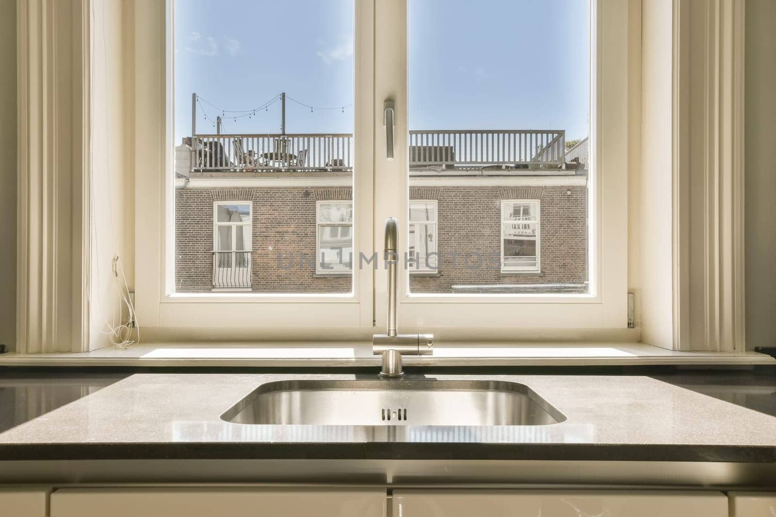 a kitchen sink in front of a window with the view of a brick building and blue sky through the windows