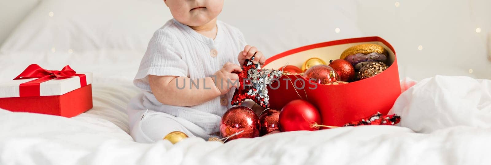 Christmas Baby in Santa Hat, Child holding christmas bauble near Present Gift Box over Holiday Lights