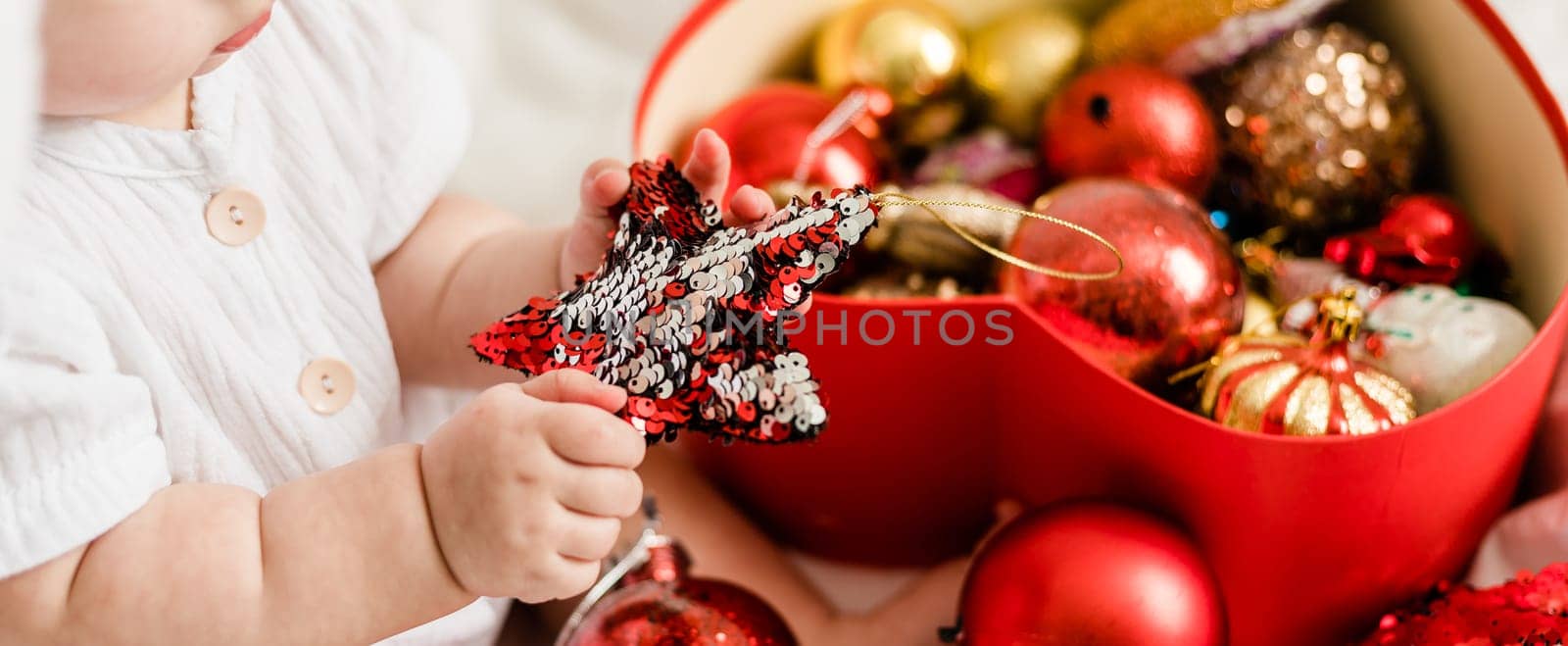 Banner Close-up Christmas Baby in Santa Hat, Child holding christmas bauble near Present Gift Box over Holiday Lights background by Satura86