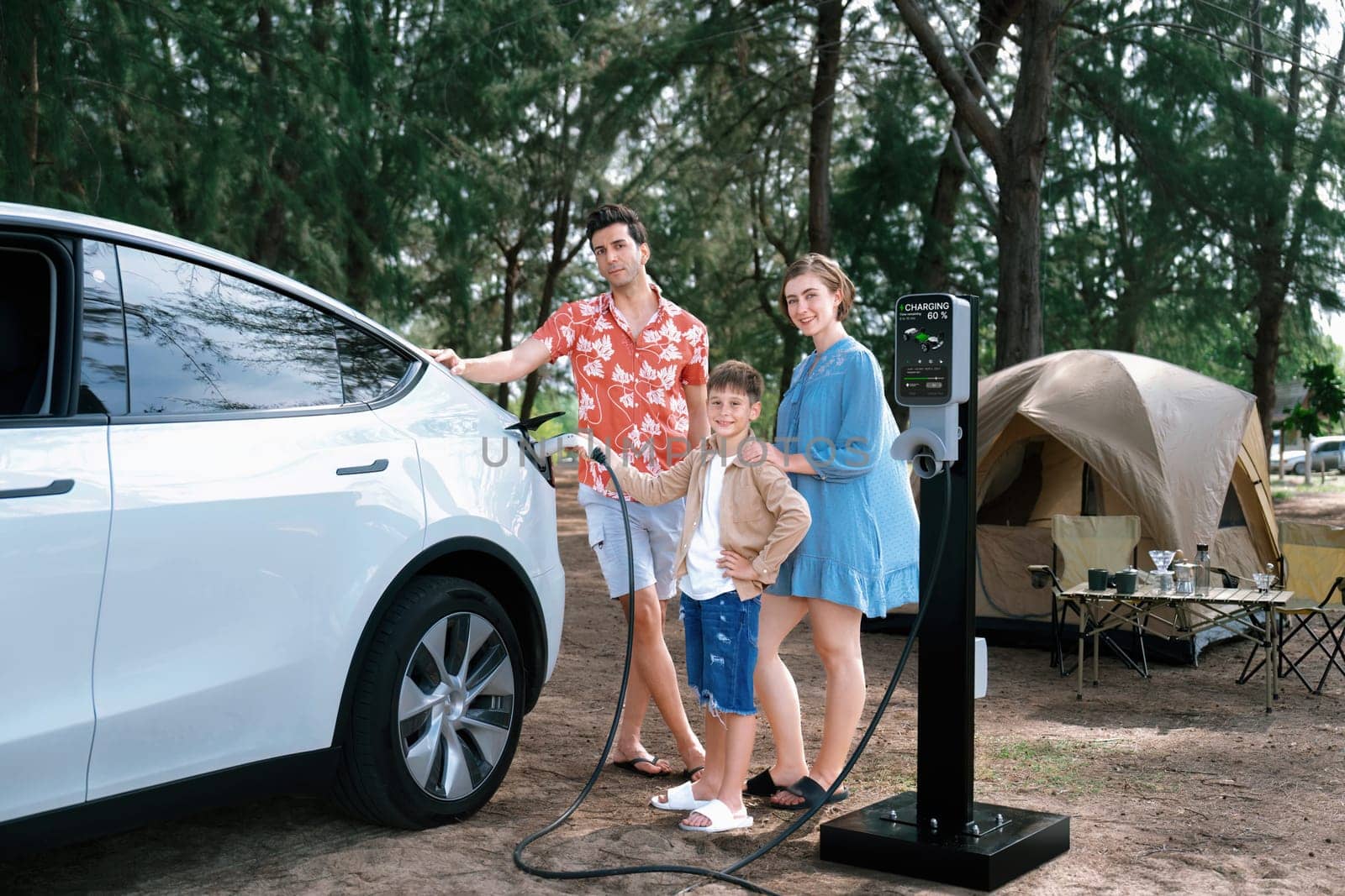 Outdoor adventure and family vacation camping in nature travel by eco friendly car for sustainable future. Lovely family recharge EV car with EV charging station in campsite. Perpetual