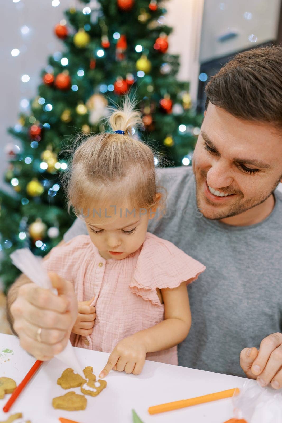 Little girl touches a cookie with her finger that her dad glazes at the table. High quality photo