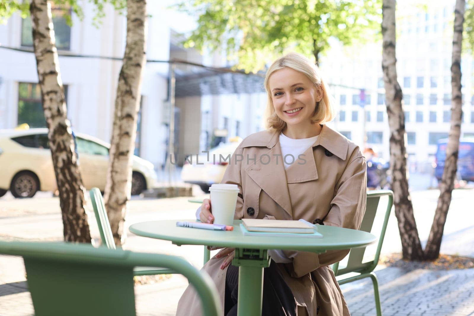 Portrait of young female student, woman with notebook, sitting in cafe and drinking coffee, smiling happily.