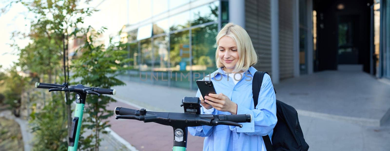 Portrait of young woman, renting a scooter, using mobile phone app to unlock it, using quick ride to get to work, smiling and looking happy by Benzoix