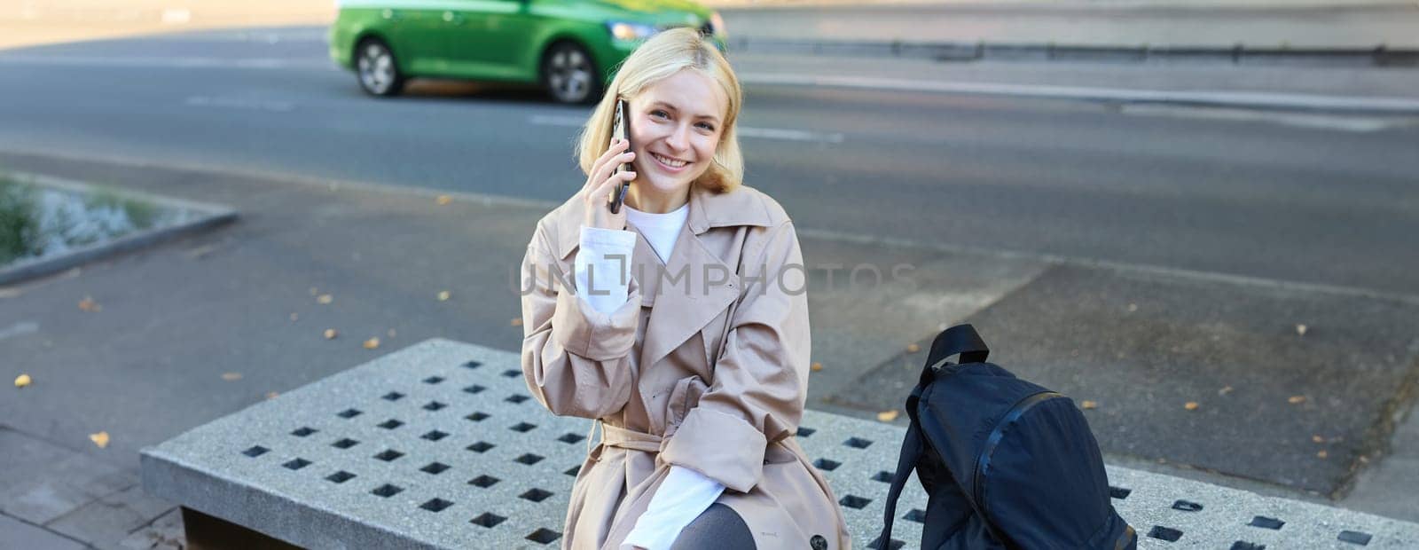 Cute young female student, woman talking on mobile phone while sitting on street bench, chatting on smartphone by Benzoix