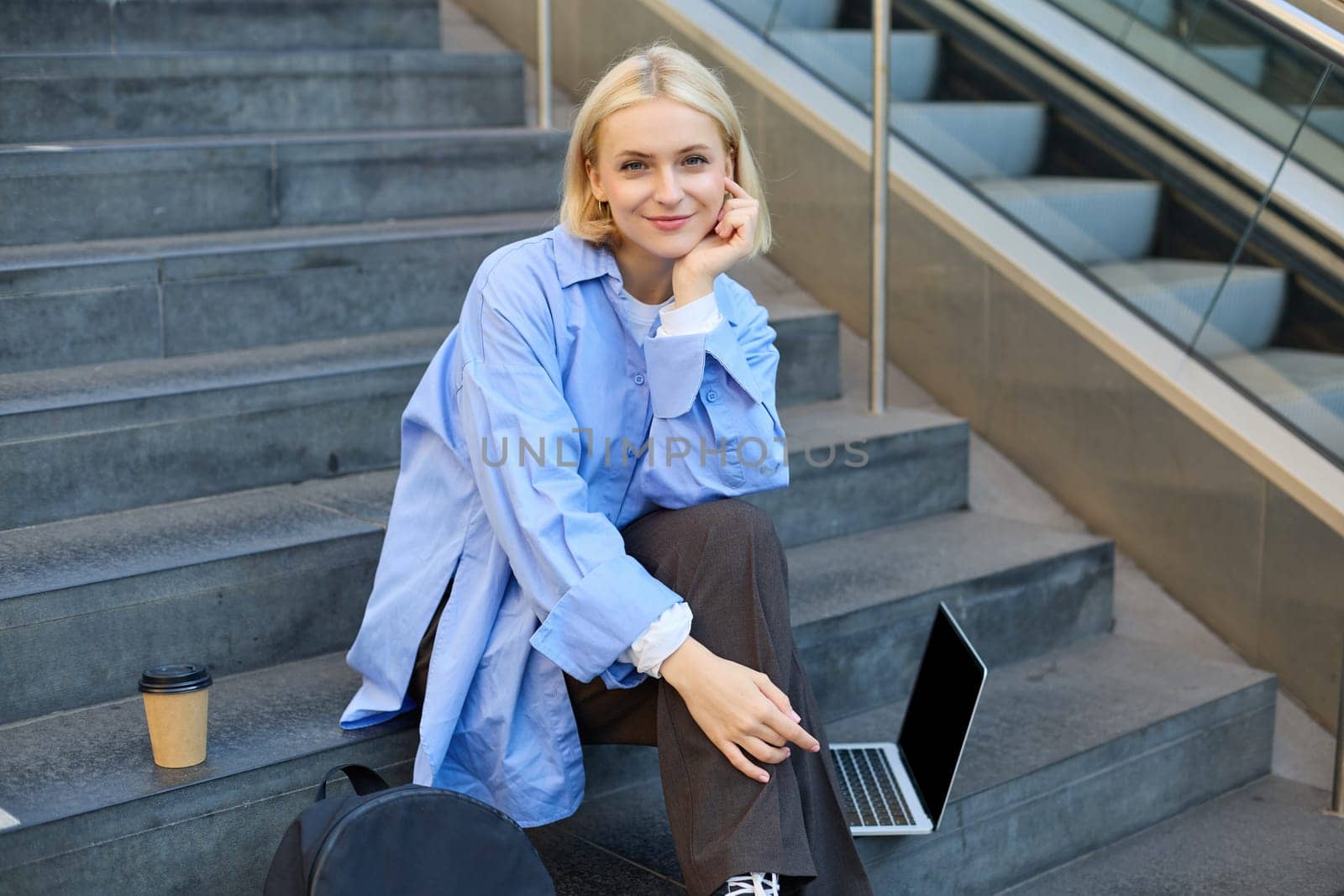 Portrait of young urban woman, college student with backpack, laptop and coffee, sitting on stairs in city, resting outdoors, taking break by Benzoix
