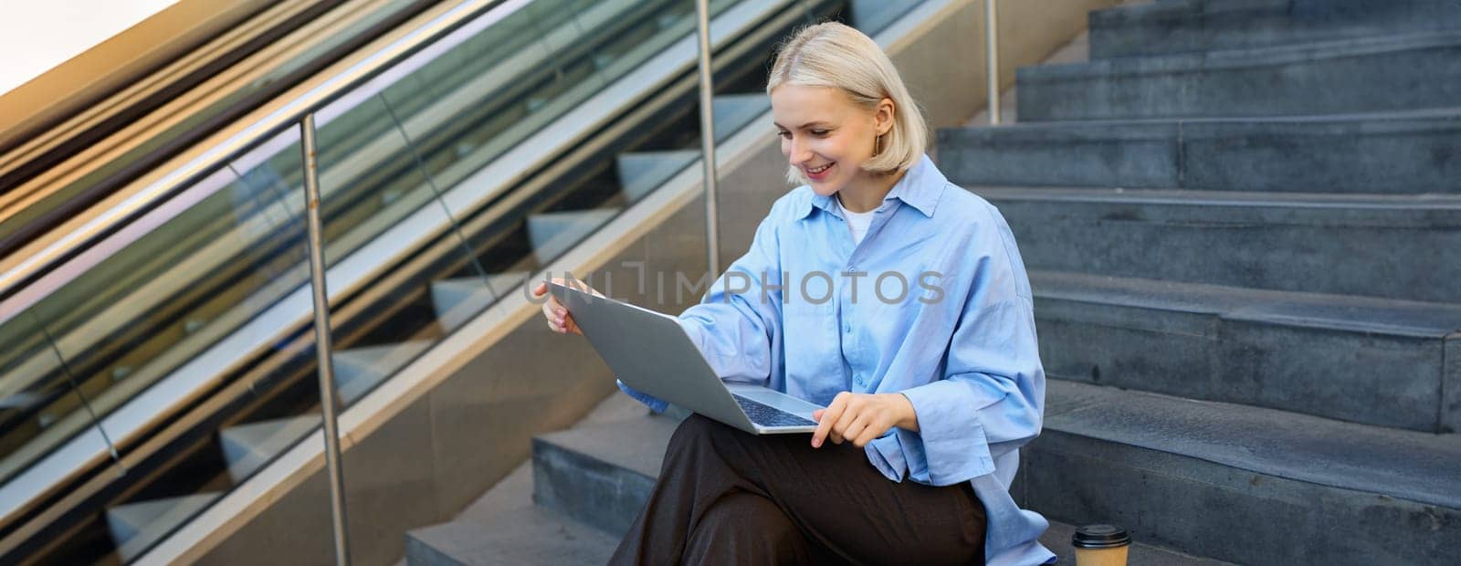 Smiling girl student using laptop computer modern technology device outdoor in university campus online learning, elearning outside sitting on urban stairs. Web education course webinars concept by Benzoix
