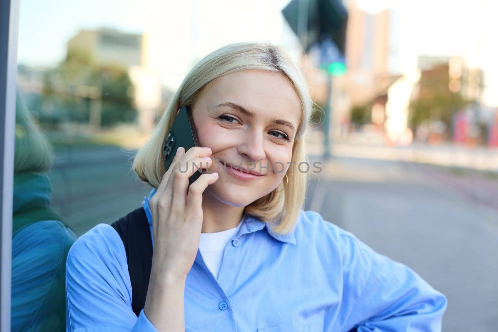 Close up portrait of smiling blond woman, chatting on the phone, talking on mobile telephone, standing on street outdoors by Benzoix