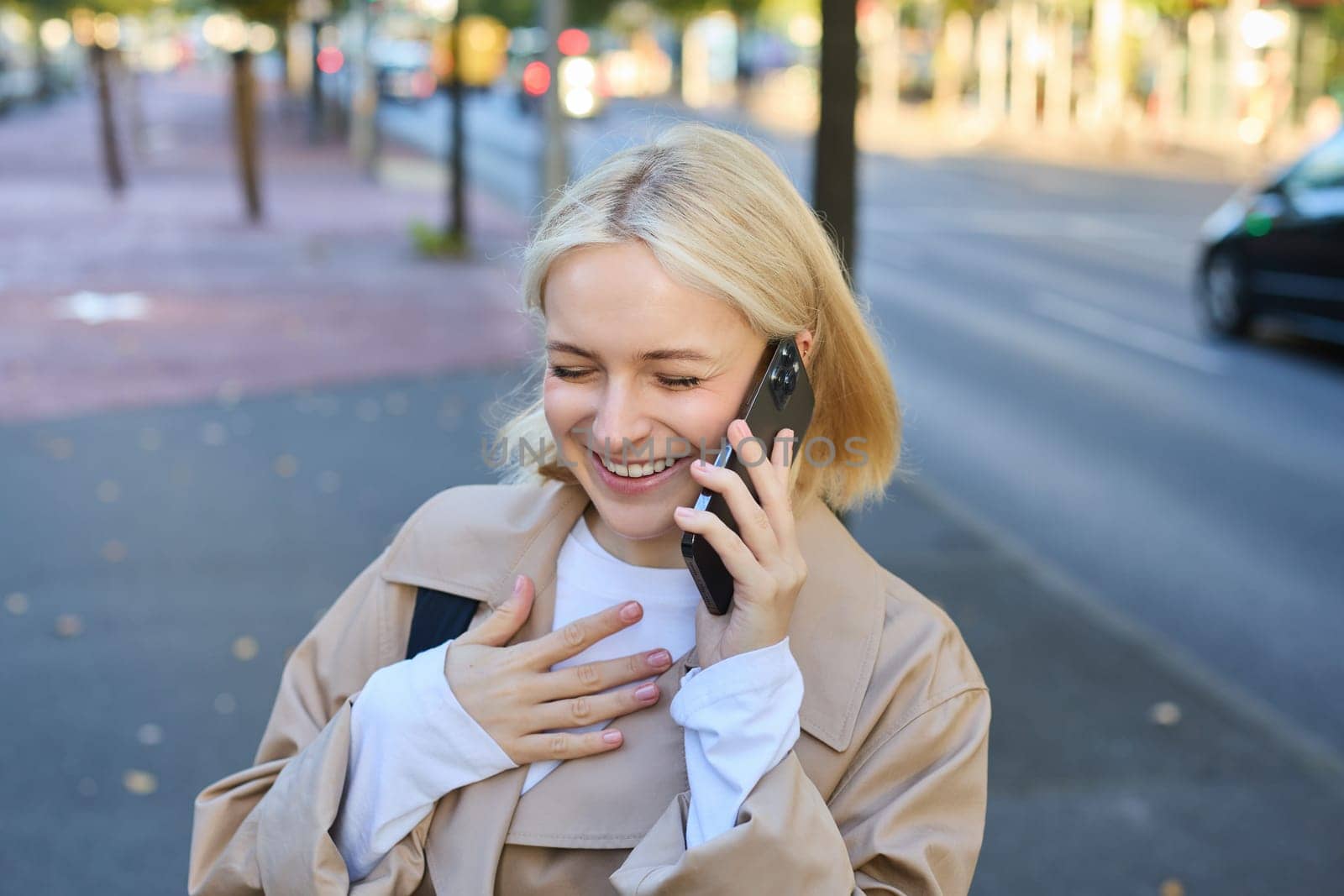 Close up portrait of smiling, happy and carefree woman on streets of big city, laughing while talking on mobile phone, chatting on smartphone and walking. Lifestyle concept