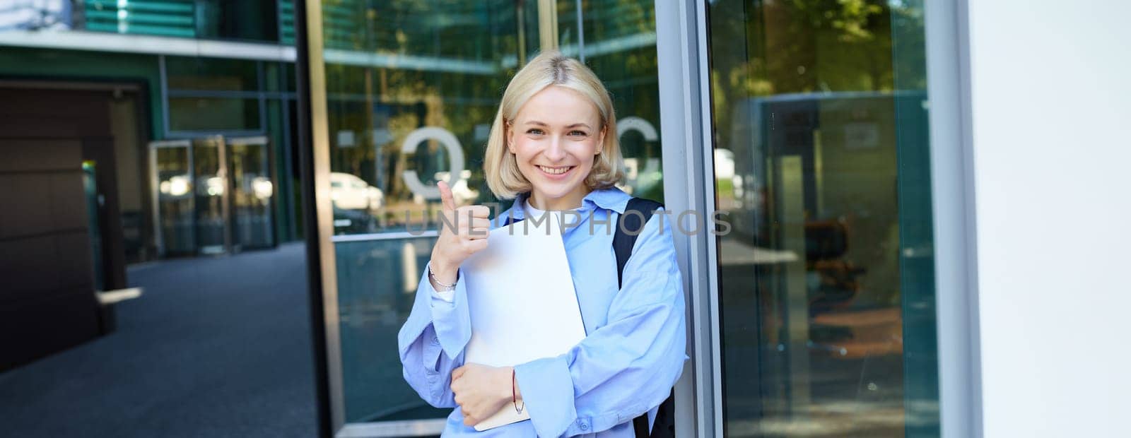 Image of young college girl, young woman with laptop, posing near university building, standing on street, smiling, concept of education and people.