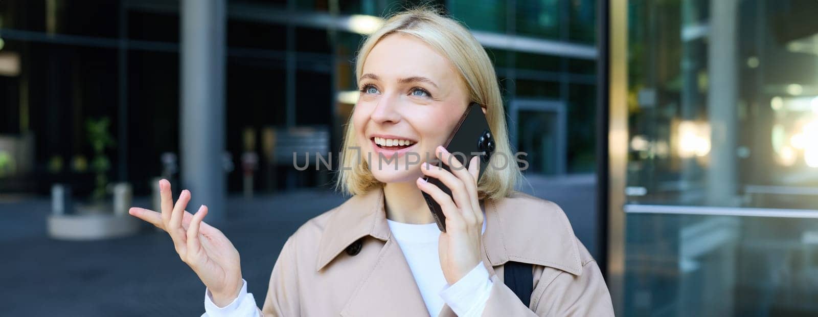 Close up portrait of young blond woman, walking on street and talking on mobile phone, chatting with friend on smartphone by Benzoix