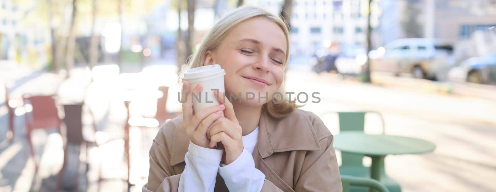 Close up portrait of smiling, happy beautiful european woman, sitting in cafe and enjoying cup of coffee, drinking beverage, enjoying bright sunny day outdoors.