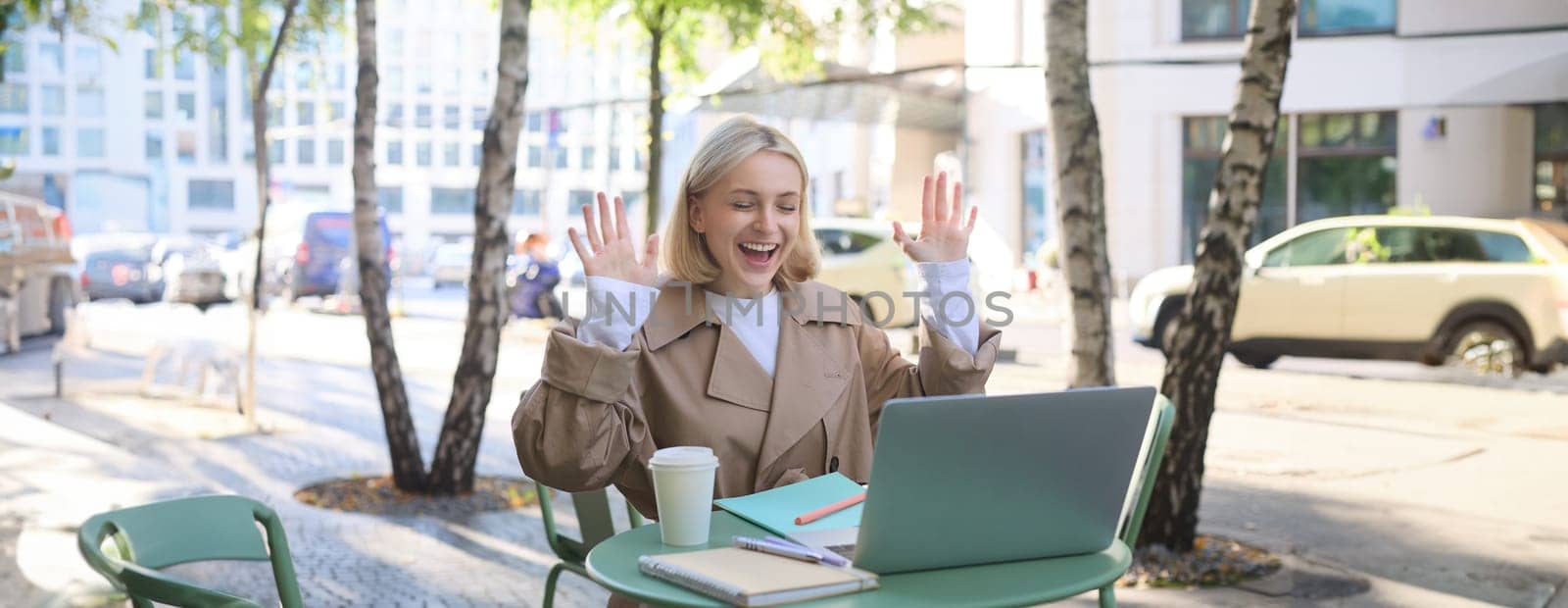 Enthusiastic young woman, carefree girl celebrating, sitting in outdoor cafe with laptop, raising hands up and laughing, triumphing by Benzoix