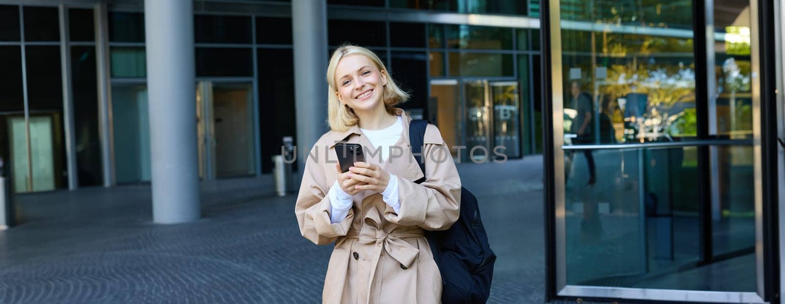 Portrait of young stylish woman walking in city centre with smartphone, using mobile phone app outdoors, waiting for someone, going to work by Benzoix