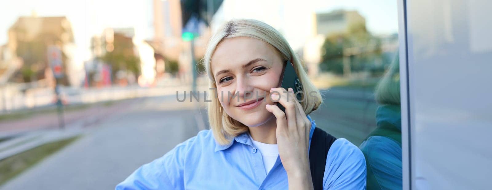 Close up portrait of smiling blond woman, chatting on the phone, talking on mobile telephone, standing on street outdoors.