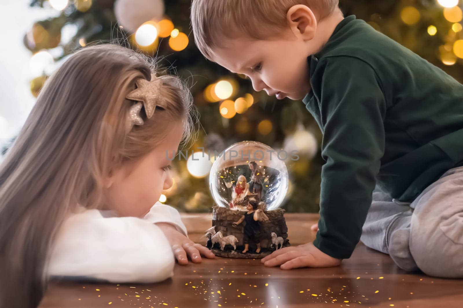 Sister and brother looking at a glass ball with a scene of the nativity of Jesus Christ in a glass ball