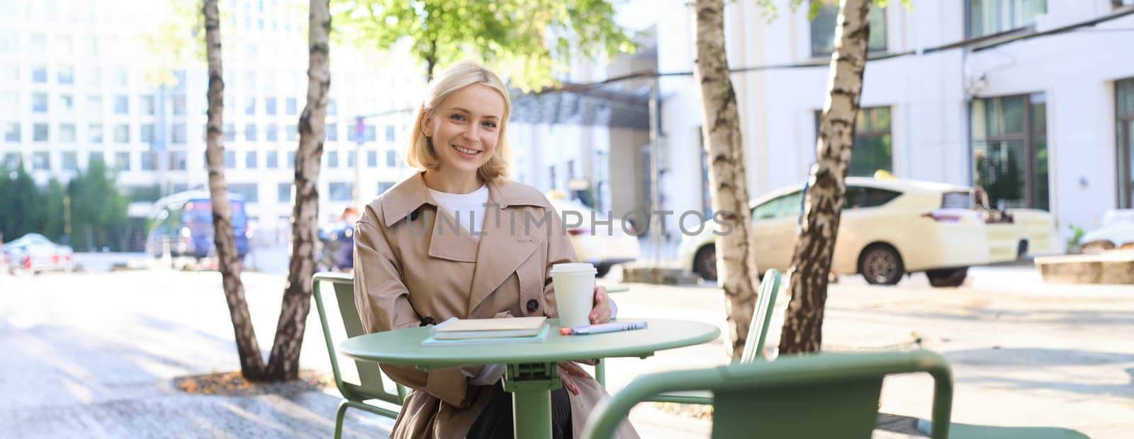 Portrait of young female student, woman with notebook, sitting in cafe and drinking coffee, smiling happily by Benzoix