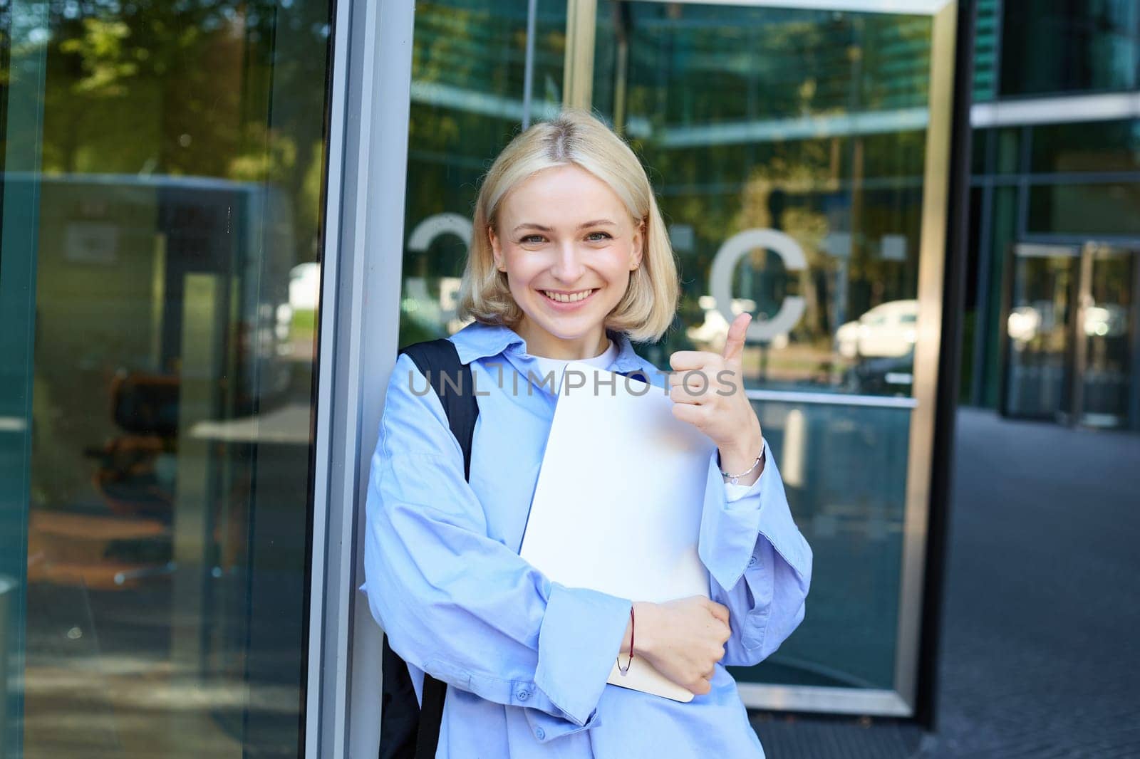 Image of young college girl, young woman with laptop, posing near university building, standing on street, smiling, concept of education and people.