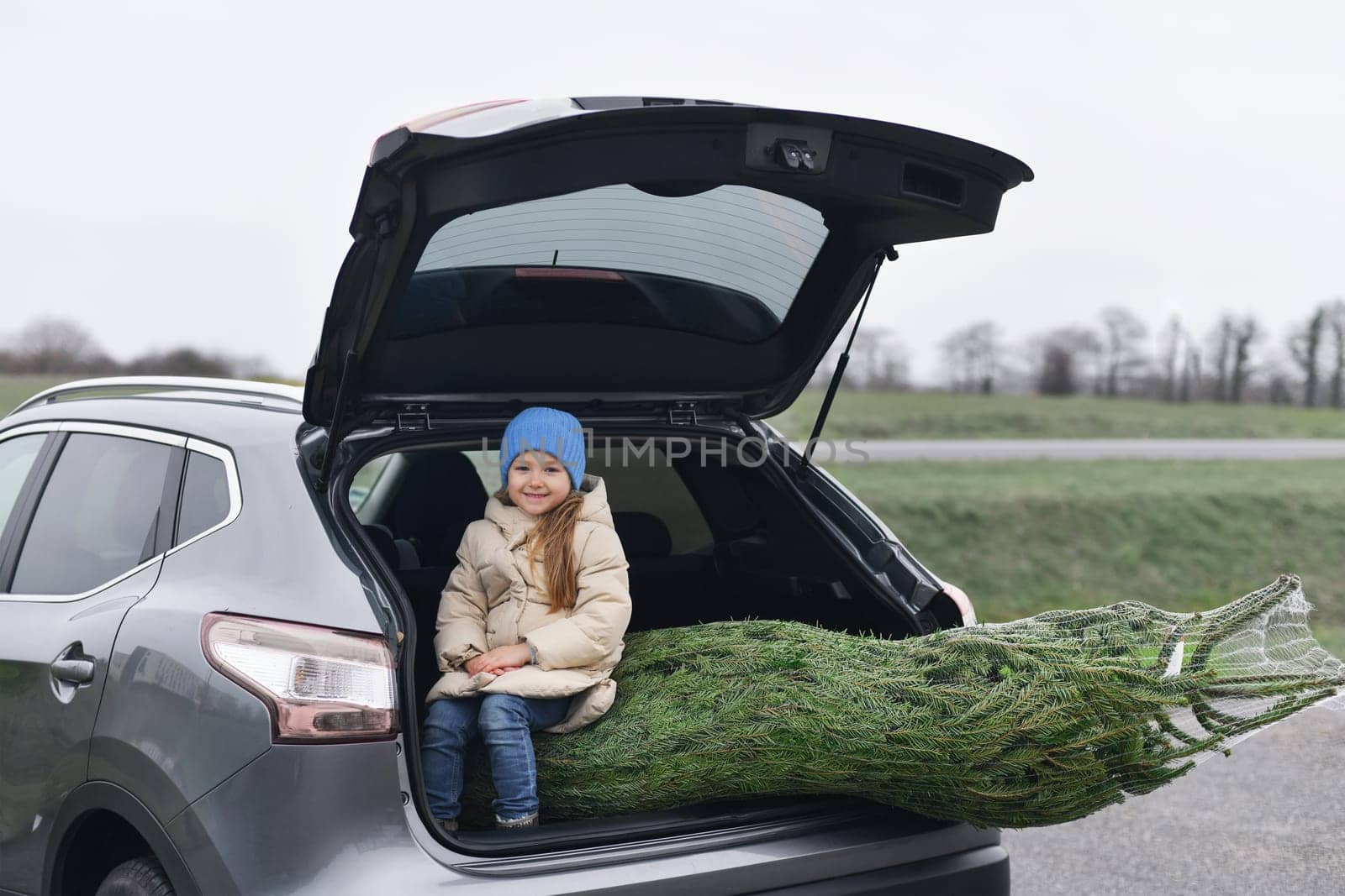 A girl sitting in the trunk with a Christmas tree