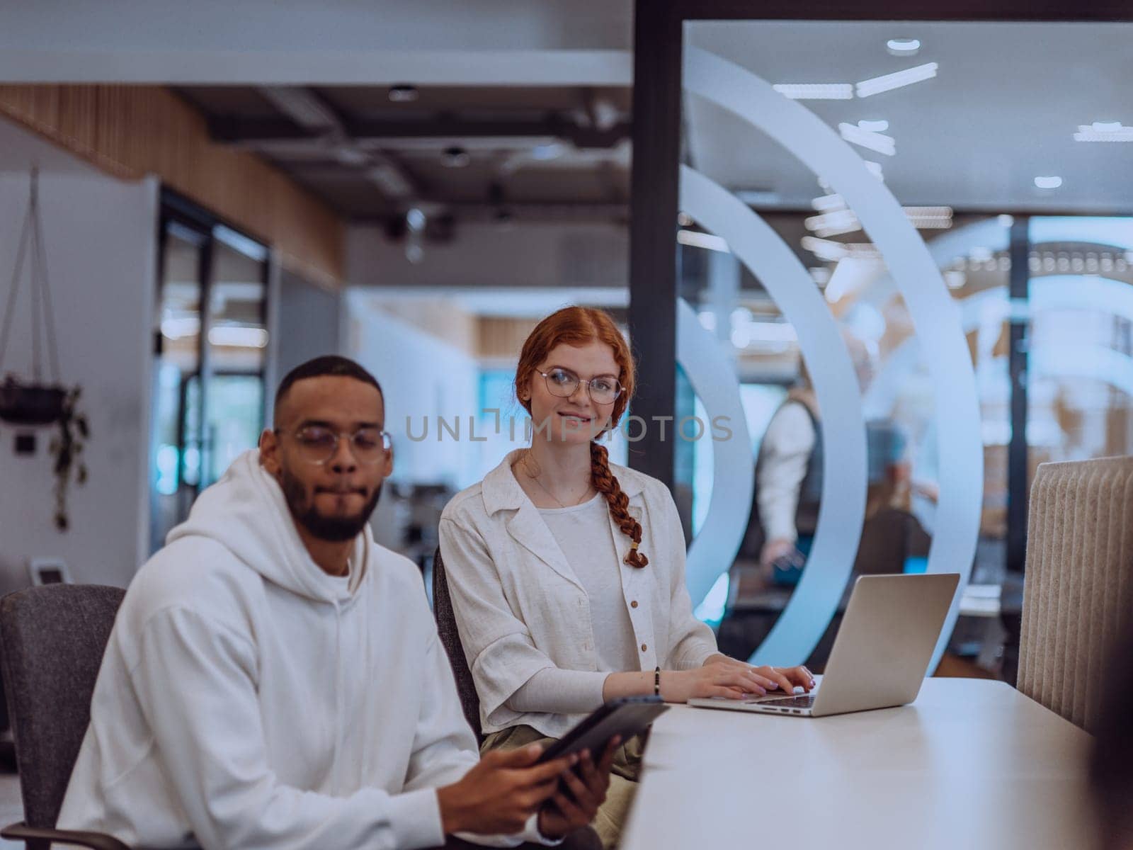 In a modern office setting, an African American businessman and his Muslim colleague, wearing a hijab, engage in collaborative discussions, tackling various business tasks and solving problems together, showcasing diversity, ambition, and teamwork in their dynamic and inclusive workplace