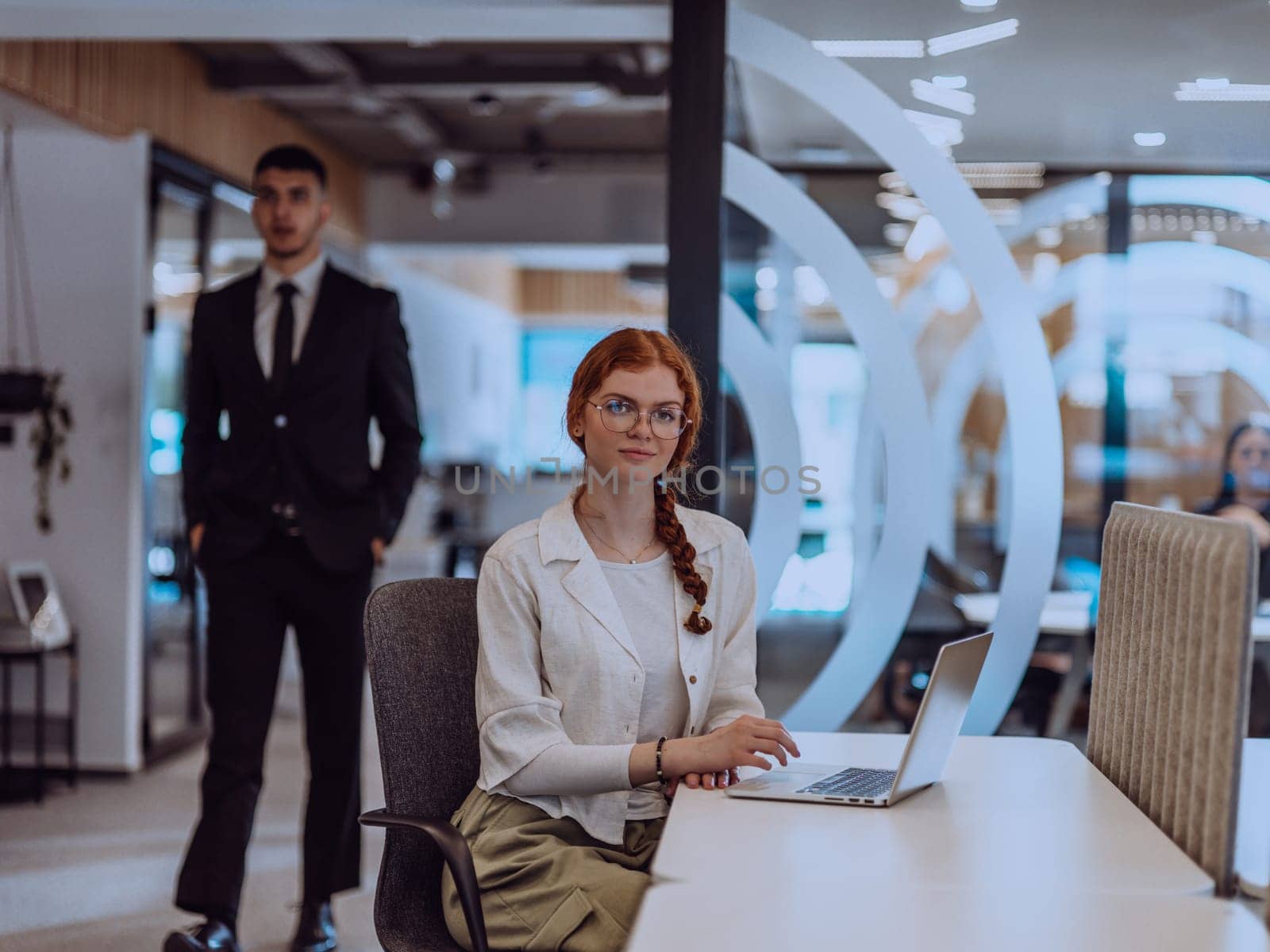 A young businesswoman with orange hair sitting confidently, fully engaged in her work on the laptop, exuding creativity, ambition, and a vibrant sense of individuality.